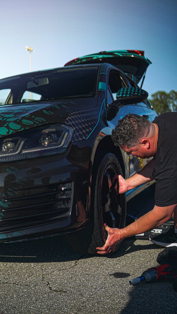 Expert mechanic changing tire on sleek black sports car under clear sky.