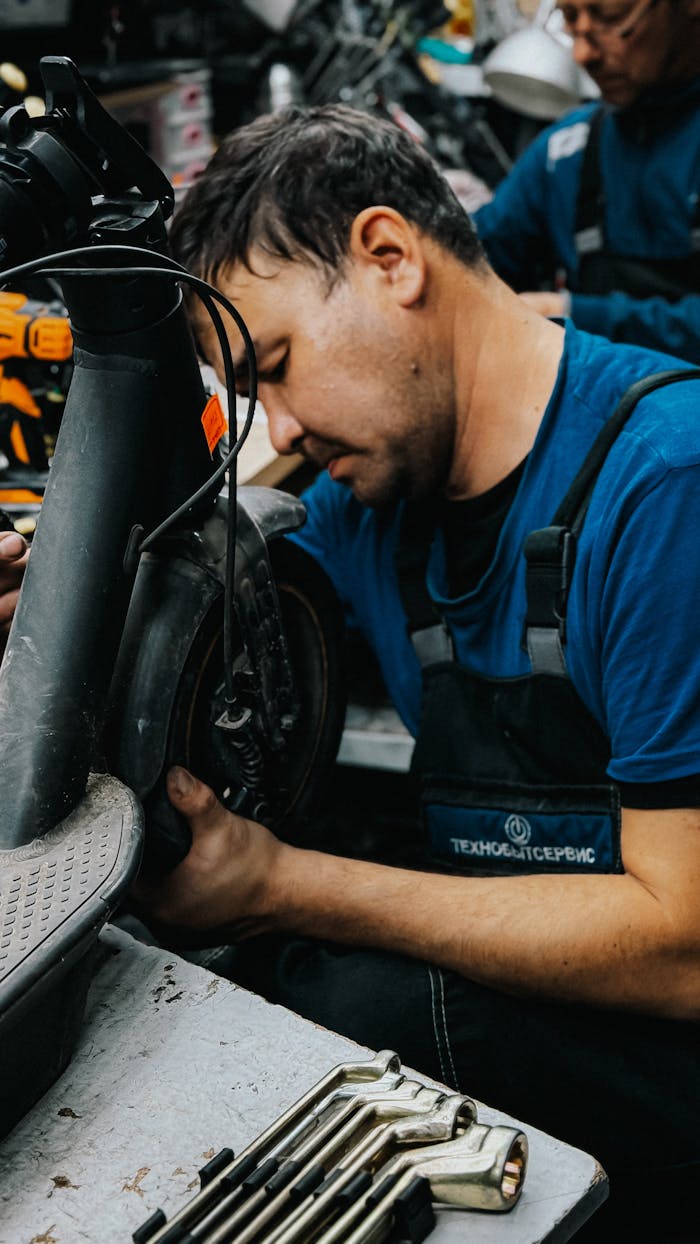 Mechanic focused on repairing an electric scooter in a busy workshop environment.